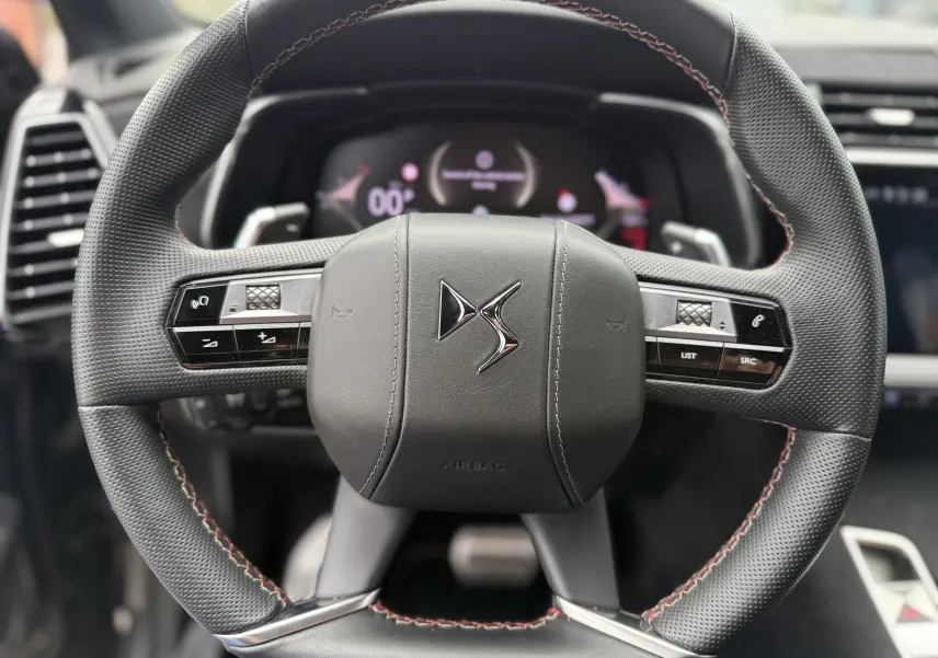 Gros plan sur le volant en cuir noir avec surpiqûres rouges du DS7 2025, mettant en valeur les commandes intégrées.