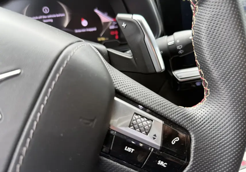 Gros plan sur le volant en cuir perforé avec surpiqûres rouges du DS7 2025, montrant les commandes intégrées.