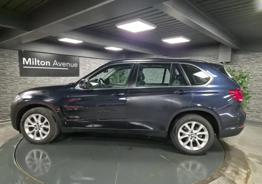 BMW X5 sDrive 25d bleu métallisé vue de profil côté gauche avec jantes alliage 19 pouces en intérieur showroom.