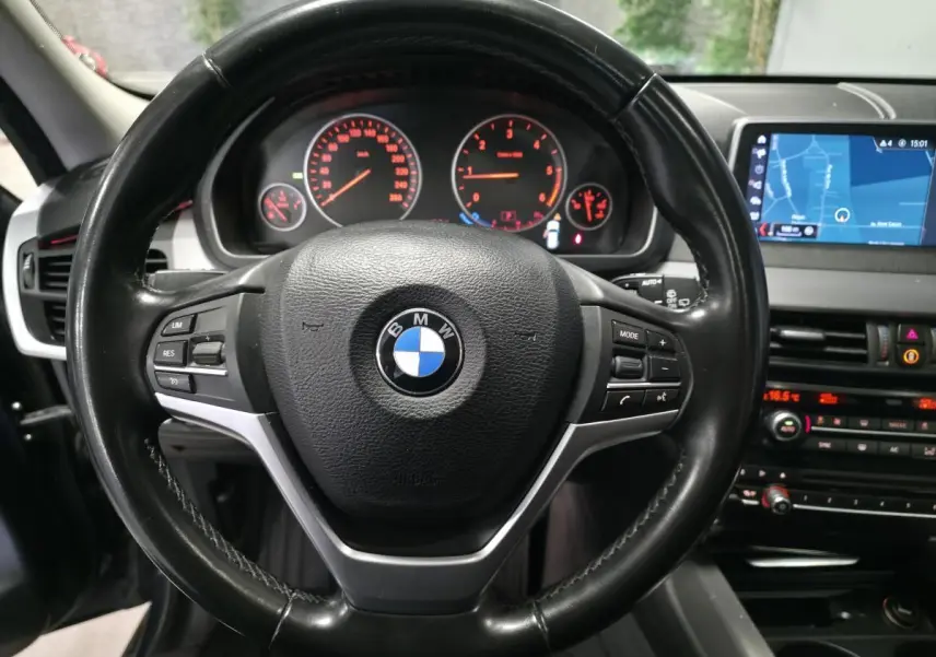Vue rapprochée du volant cuir noir BMW avec tableau de bord et écran de navigation dans un X5 sDrive 25d 2018.