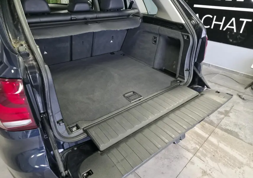 Coffre ouvert vu de l'arrière d'un BMW X5 sDrive 25d bleu avec plancher de chargement déplié et sellerie noire.