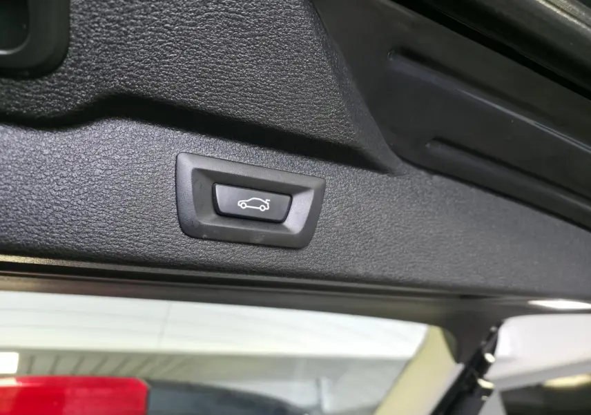 Bouton d'ouverture électrique du hayon vu en gros plan sur le bord intérieur du coffre d'un BMW X5 bleu 2018.