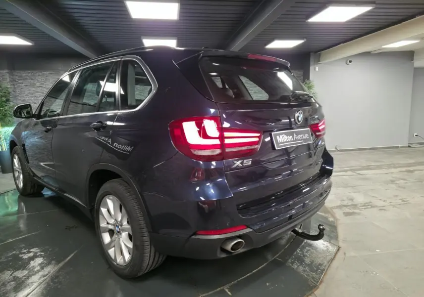 Vue 3/4 arrière droite d'un BMW X5 bleu métallisé avec crochet d'attelage et jantes alliage 19 pouces en showroom.