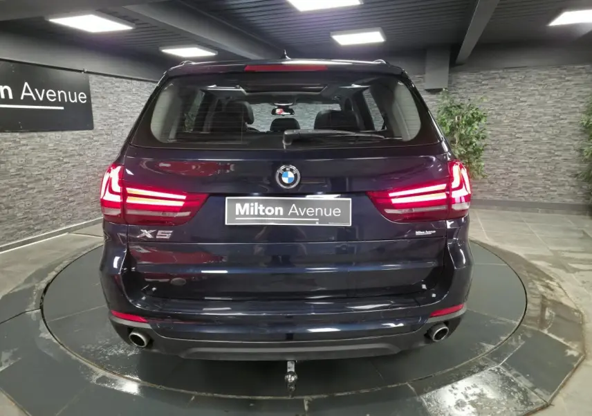 Vue arrière d'un BMW X5 sDrive 25d bleu métallisé avec feux LED allumés et crochet d'attelage démontable.