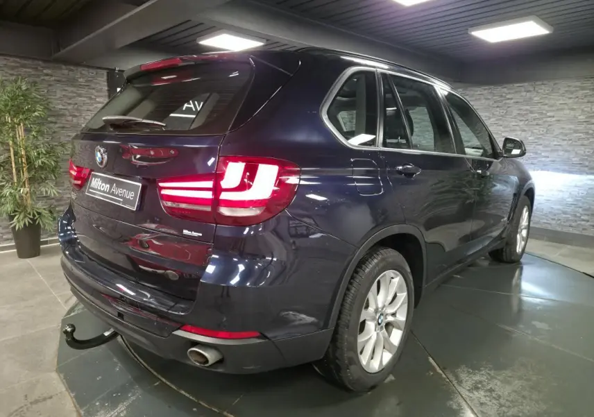 Vue 3/4 arrière droite d'un BMW X5 sDrive 25d bleu métallisé avec crochet d'attelage et jantes alliage 19 pouces.