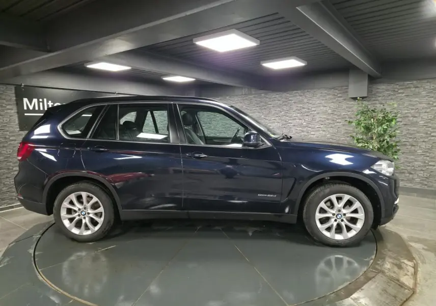 Profil droit d’un BMW X5 sDrive 25d bleu métallisé avec jantes alliage 19 pouces dans un showroom.