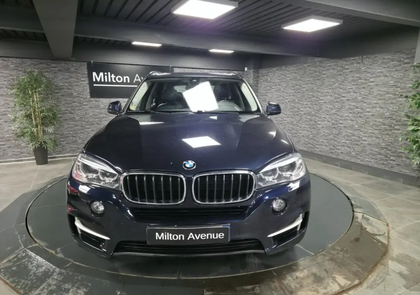 BMW X5 sDrive 25d bleu métallisé vue de face avec calandre noire et projecteurs bi-xénon allumés.