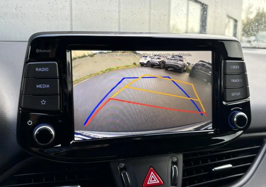 Écran tactile de la Hyundai i30 SW T-GDI 120 Modern affichant la caméra de recul avec lignes de guidage colorées.