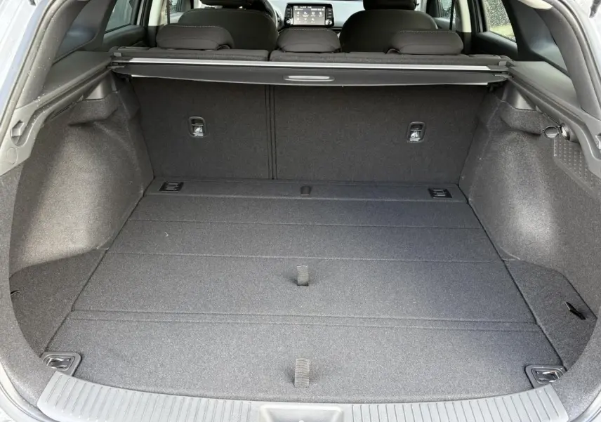 Coffre ouvert vu de l'arrière d'une Hyundai i30 SW T-GDI 120 Modern gris argent, intérieur noir et tablette de séparation.
