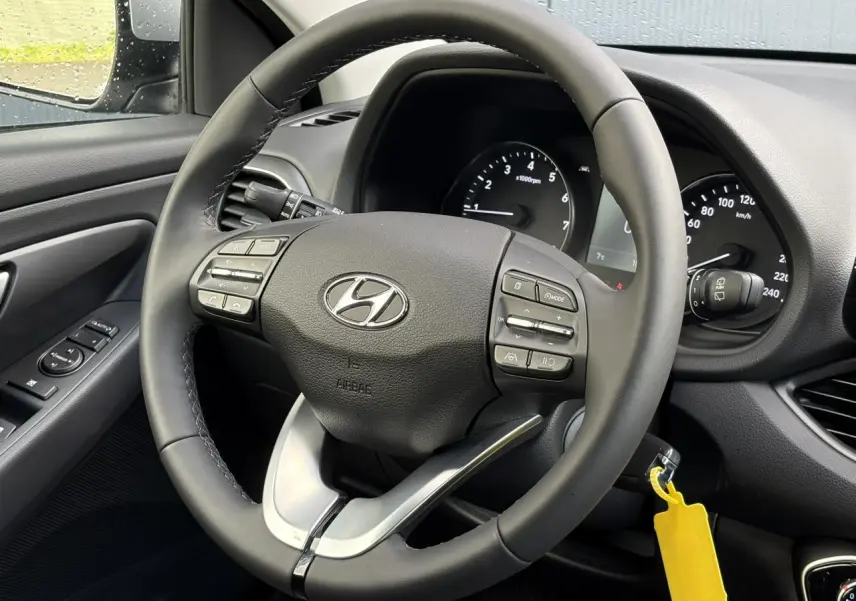 Vue rapprochée du volant cuir noir de la Hyundai i30 SW T-GDI 120 Modern avec commandes intégrées et tableau de bord visible.