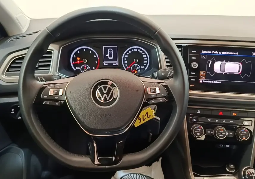 Vue intérieure centrée sur le volant cuir multifonctions d’un Volkswagen T-Roc 1.5 TSI avec tableau de bord digital et écran tactile.