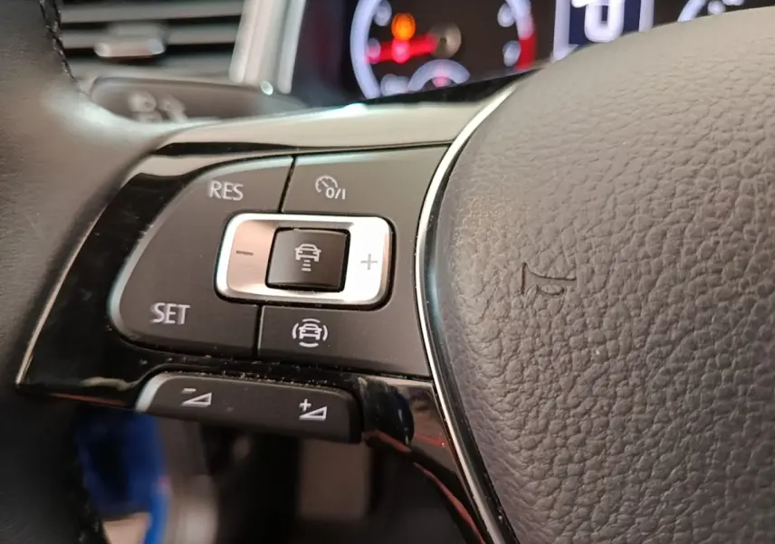 Gros plan sur les commandes du régulateur adaptatif au volant cuir noir du Volkswagen T-Roc bleu, tableau de bord en arrière-plan.