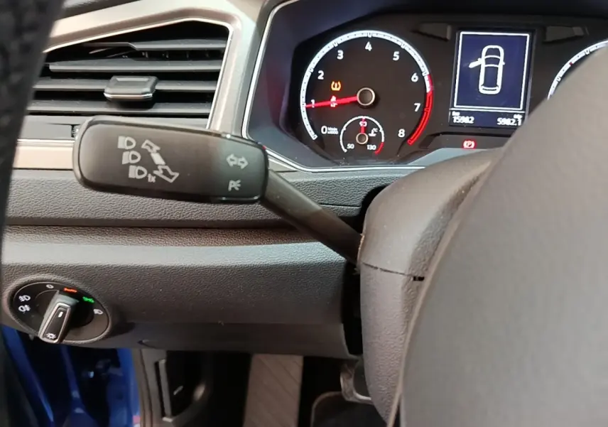 Vue rapprochée du tableau de bord et du commodo gauche du Volkswagen T-Roc bleu, avec compteurs et voyants visibles.