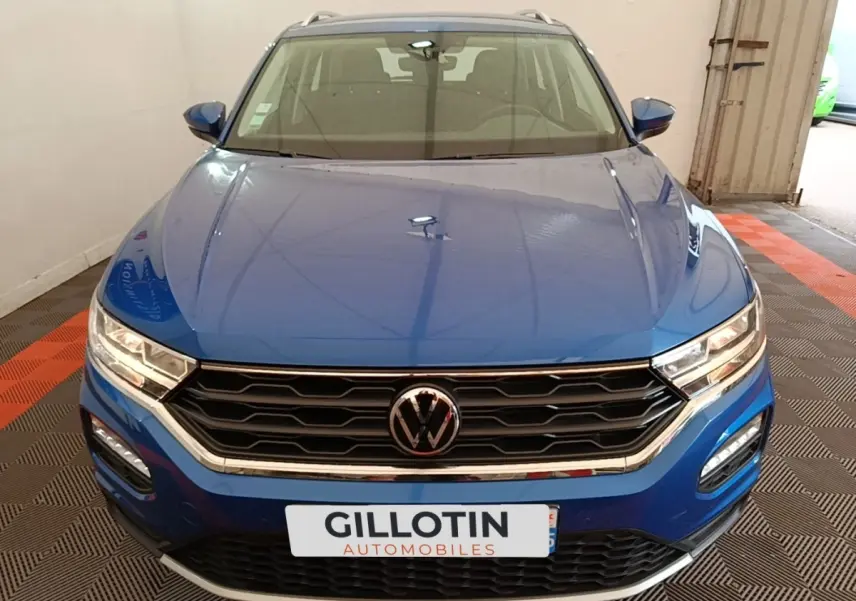 Vue avant d’un Volkswagen T-Roc bleu 2020 avec calandre noire et phares LED allumés dans un garage.