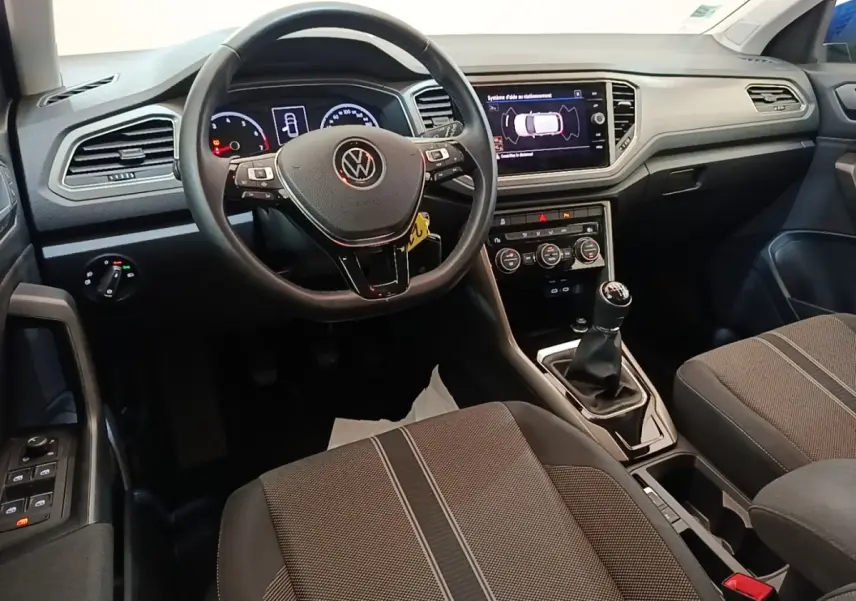 Vue intérieure avant du Volkswagen T-Roc 1.5 TSI bleu, volant cuir multifonctions et boîte manuelle visible.