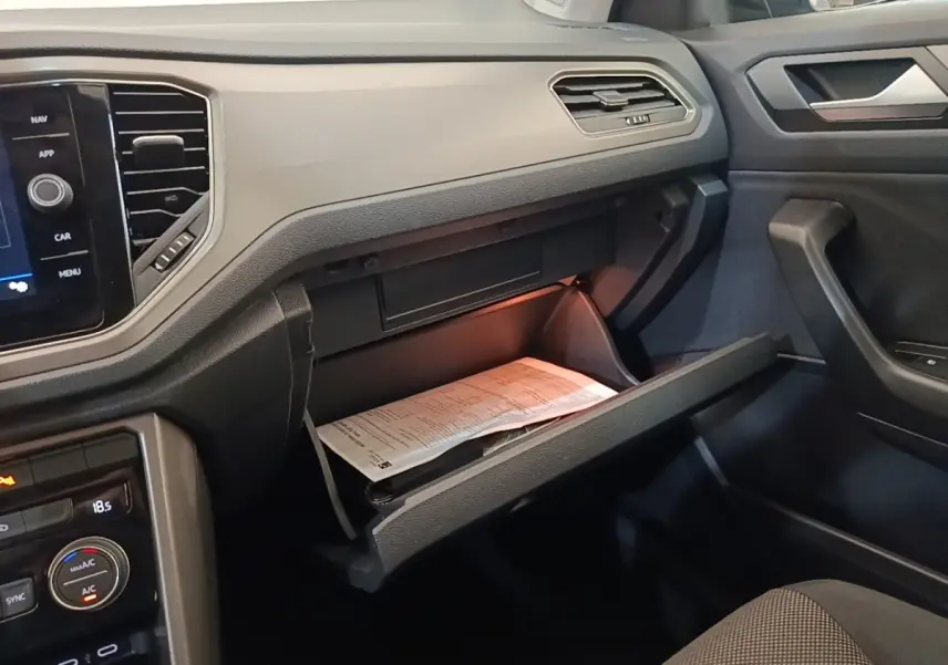 Vue intérieure côté passager du tableau de bord noir du Volkswagen T-Roc avec boîte à gants ouverte et documents visibles.