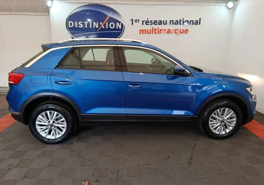 Profil droit d’un Volkswagen T-Roc bleu 2020 avec toit blanc et jantes alliage, en intérieur showroom.