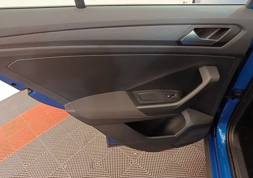 Vue rapprochée de la porte avant gauche bleu vif d’un Volkswagen T-Roc 1.5 TSI avec poignée et bouton de vitre électrique.
