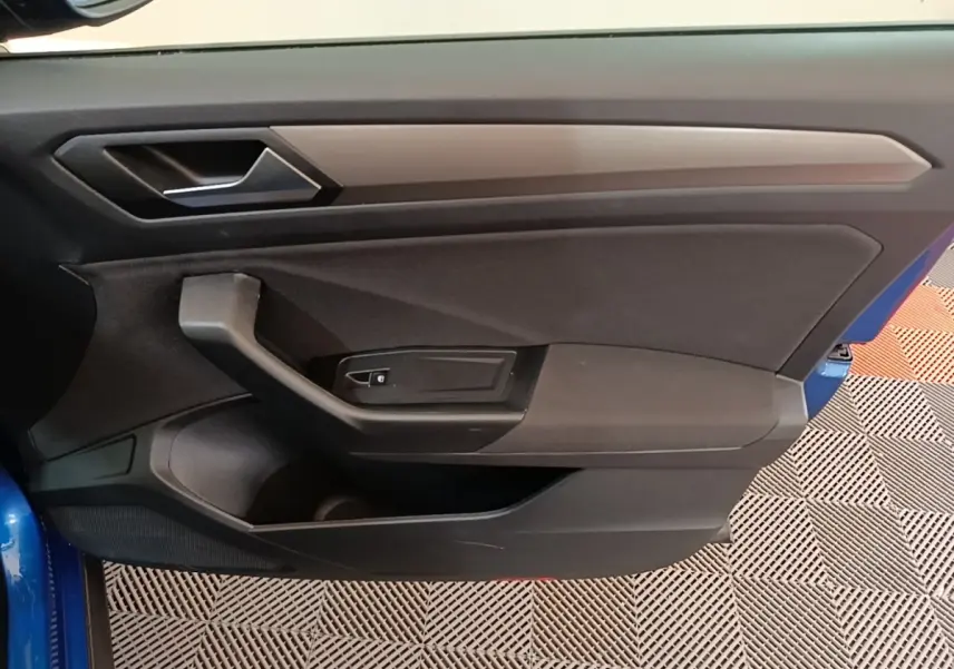 Vue intérieure de la porte avant gauche d’un Volkswagen T-Roc bleu, avec poignée et commande de vitre noire.