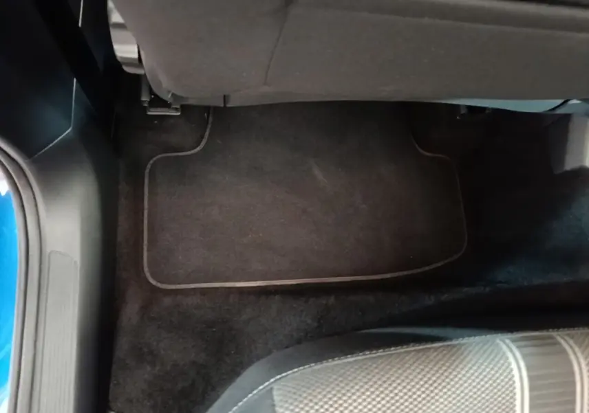 Vue intérieure du plancher arrière côté gauche du Volkswagen T-Roc bleu, avec tapis de sol noir et siège tissu gris.