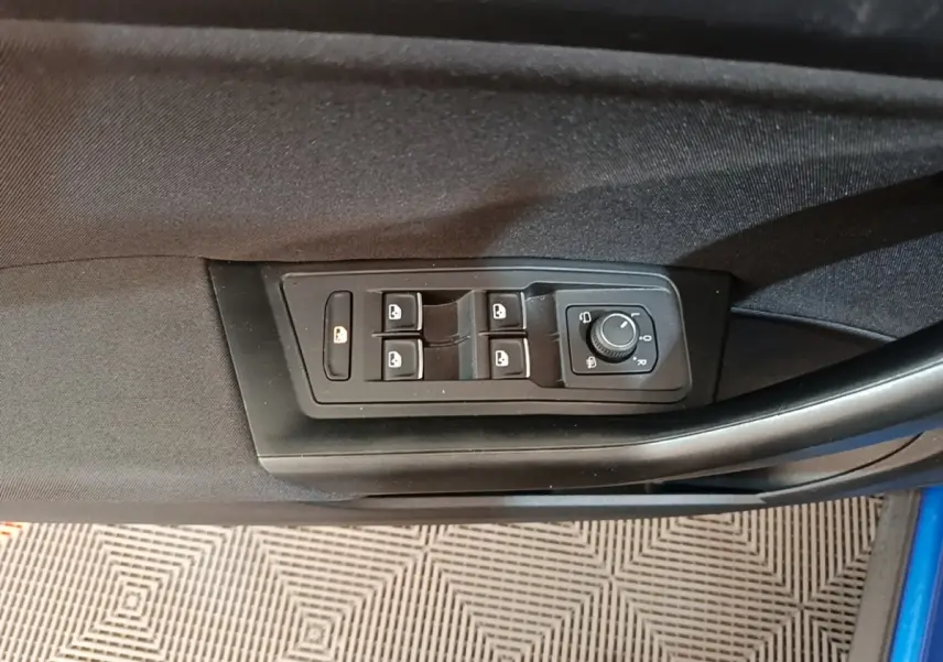 Vue rapprochée des commandes des vitres et rétroviseurs sur la porte côté conducteur du Volkswagen T-Roc bleu.