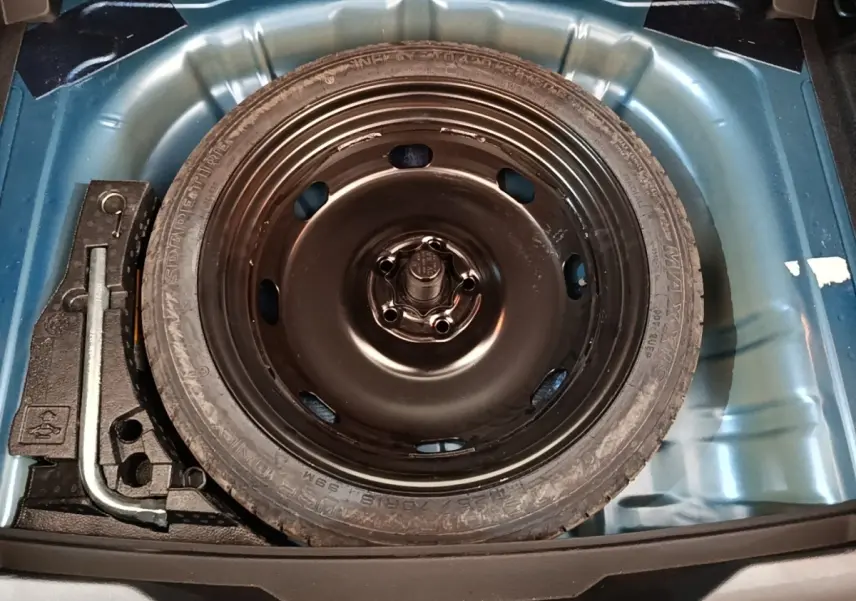 Roue de secours noire dans le coffre bleu d’un Volkswagen T-Roc 1.5 TSI 150 EVO UNITED, vue de dessus.
