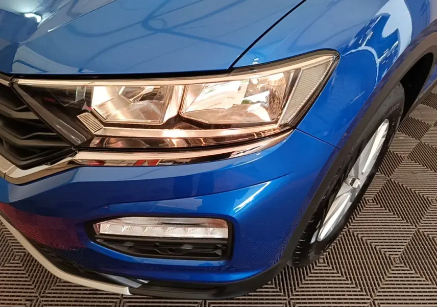 Gros plan sur l'avant droit bleu du Volkswagen T-Roc 1.5 TSI 150 EVO UNITED, mettant en valeur les phares et la calandre.