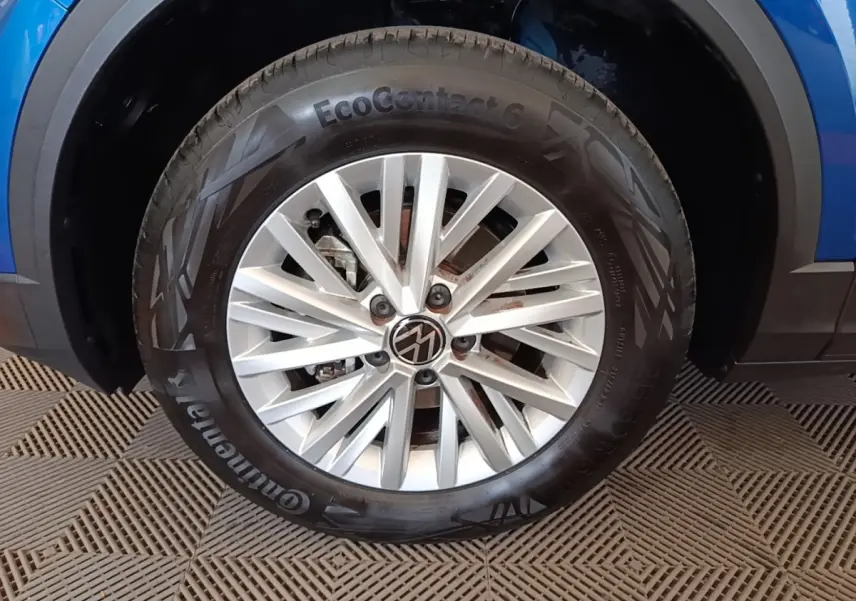 Gros plan sur la roue avant droite d’un Volkswagen T-Roc bleu, jante alliage argentée avec logo VW central.