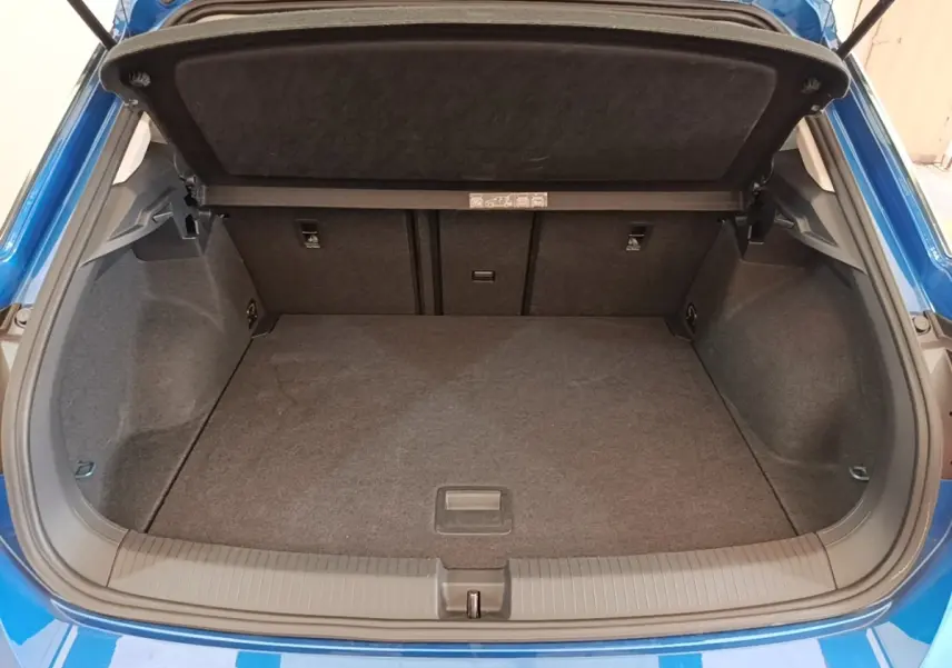 Coffre ouvert vu de l'arrière d'un Volkswagen T-Roc bleu 1.5 TSI 150 EVO UNITED, espace de chargement vide et tapis gris.