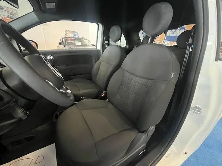 Vue intérieure côté conducteur de la Fiat 500 blanche 2023, avec sièges noirs et volant visible.