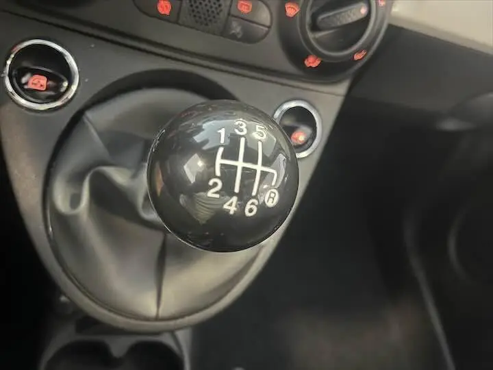 Gros plan sur le levier de vitesses manuel noir de la FIAT 500 blanche, avec commandes de climatisation en arrière-plan.