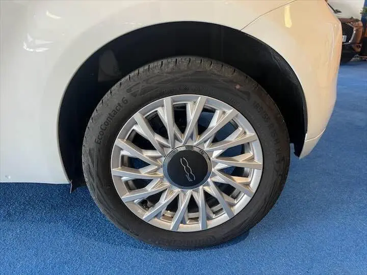 Gros plan sur la roue avant droite d'une FIAT 500 blanche, mettant en valeur la jante argentée au design étoilé.