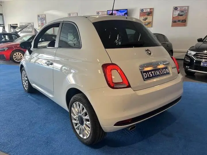 Vue 3/4 arrière droite d'une FIAT 500 blanche 2023 en showroom avec jantes alliage et feux arrière LED.