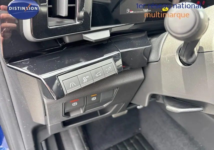 Gros plan sur les commandes sous le tableau de bord du Renault Austral bleu Iron Metal, avec boutons d'assistance et frein à main électrique.