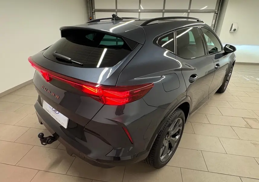 Vue 3/4 arrière droite d'un CUPRA Formentor gris magnétique avec attelage escamotable et feux arrière allumés.