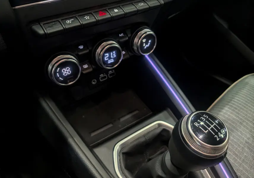 Gros plan sur la console centrale de la Renault Clio V rouge, mettant en valeur la boîte manuelle et les commandes de climatisation.