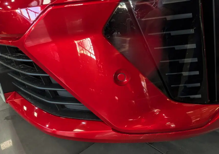 Gros plan sur le bouclier avant rouge flamme de la Renault Clio V ECO-100 CH TECHNO avec capteur de stationnement visible.