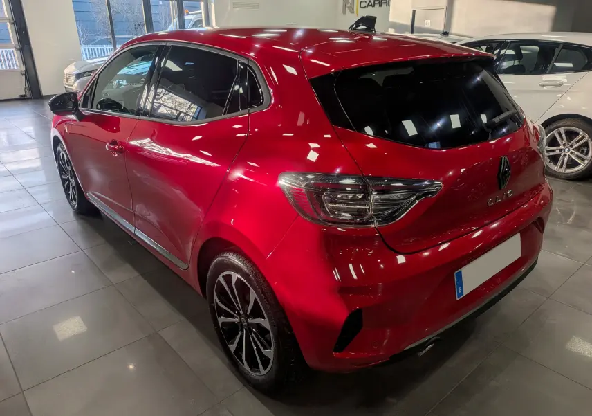 Vue 3/4 arrière droite d'une Renault Clio V rouge flamme avec jantes alliage et vitres teintées en intérieur showroom.