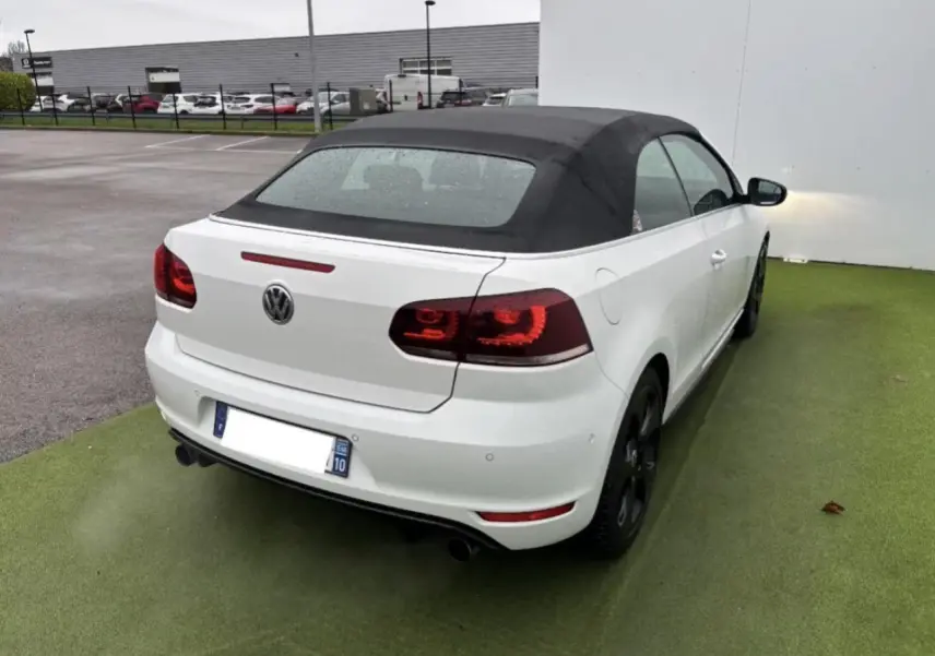 Vue 3/4 arrière droite d'une Volkswagen Golf VI Cabriolet blanche avec toit souple noir et feux arrière LED teintés.