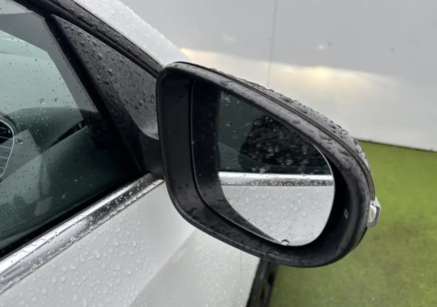 Rétroviseur côté gauche d'une Volkswagen Golf VI Cabriolet blanc avec gouttes de pluie sur la carrosserie et vitre teintée.