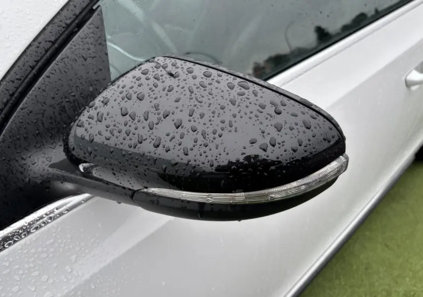 Rétroviseur noir côté gauche avec clignotant intégré sur Volkswagen Golf VI Cabriolet blanc, vue rapprochée sous la pluie.