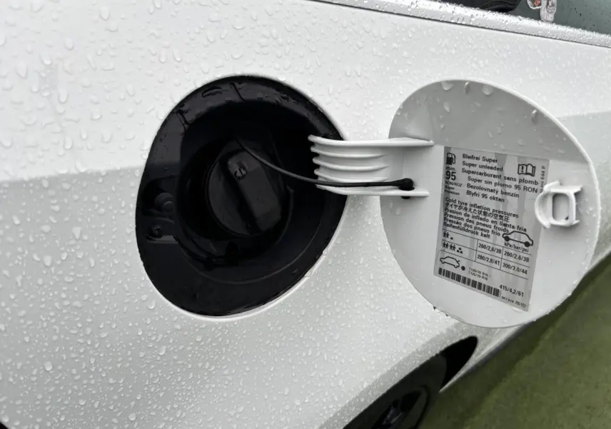 Détail de la trappe à carburant ouverte sur une Volkswagen Golf VI Cabriolet blanche, avec gouttes d'eau visibles.