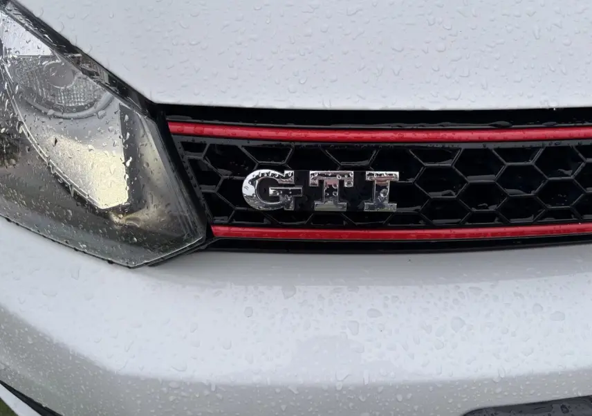Gros plan sur la calandre avant blanche d'une Volkswagen Golf VI Cabriolet GTI avec logo GTI et liseré rouge.