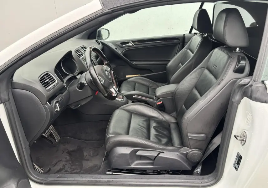 Intérieur côté conducteur d'une Volkswagen Golf VI Cabriolet blanc, sièges sport cuir noirs avec logo GTI brodé.