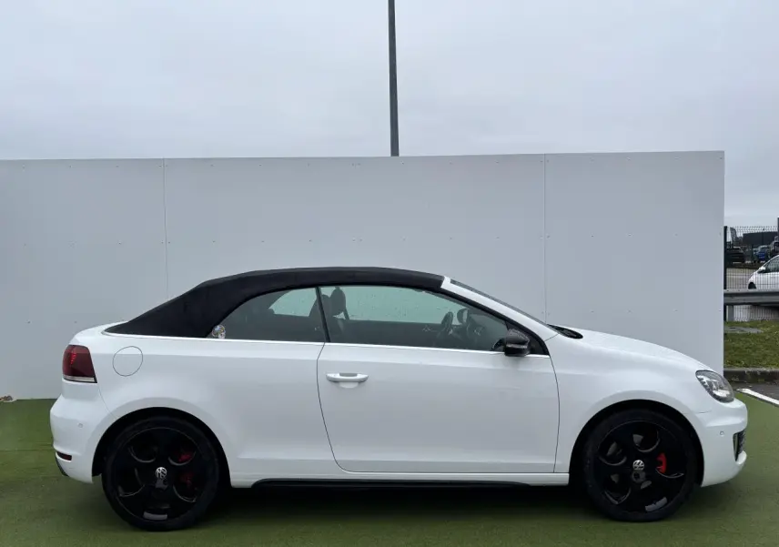 Profil droit d'une Volkswagen Golf VI Cabriolet blanche avec toit souple noir et jantes alliage noires.