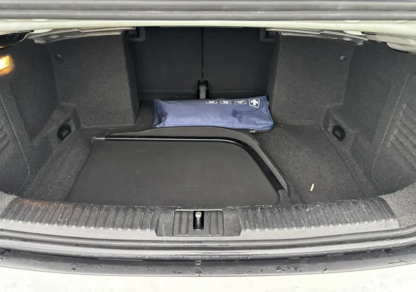 Coffre ouvert d'une Volkswagen Golf VI Cabriolet blanche, montrant un filet de séparation et une trousse de secours bleue.