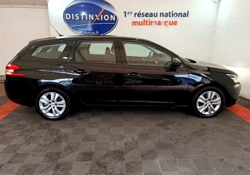 Peugeot 308 break noir vue de profil côté gauche, stationnée en intérieur avec logo Distinxion en arrière-plan.
