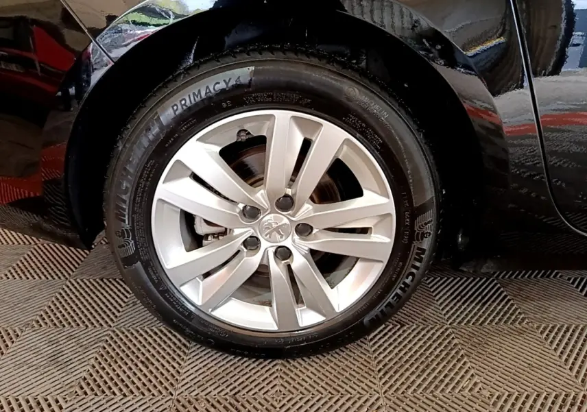 Gros plan sur la roue avant gauche d’une Peugeot 308 noire, mettant en valeur la jante alliage et le pneu Michelin.