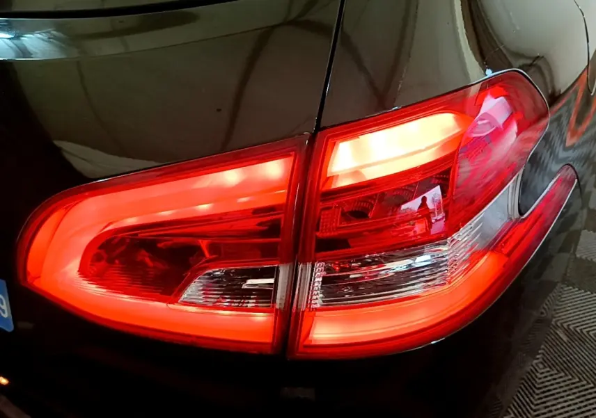 Gros plan sur le feu arrière droit rouge allumé d'une Peugeot 308 noire, reflet sur la carrosserie brillante.