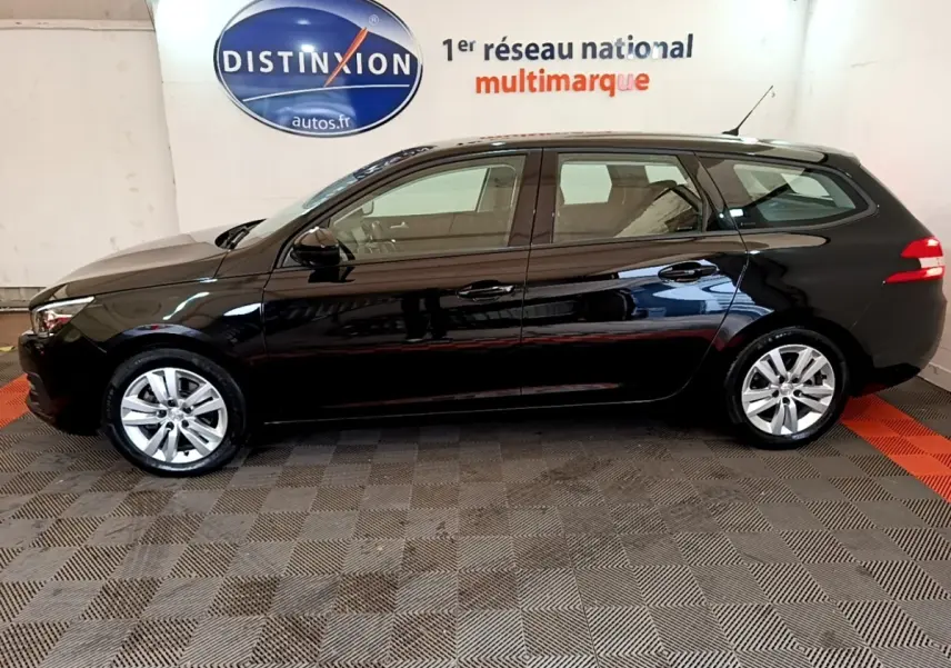 Profil droit d'une Peugeot 308 noire break de 2020, avec jantes alliage et feux arrière allumés en intérieur showroom.